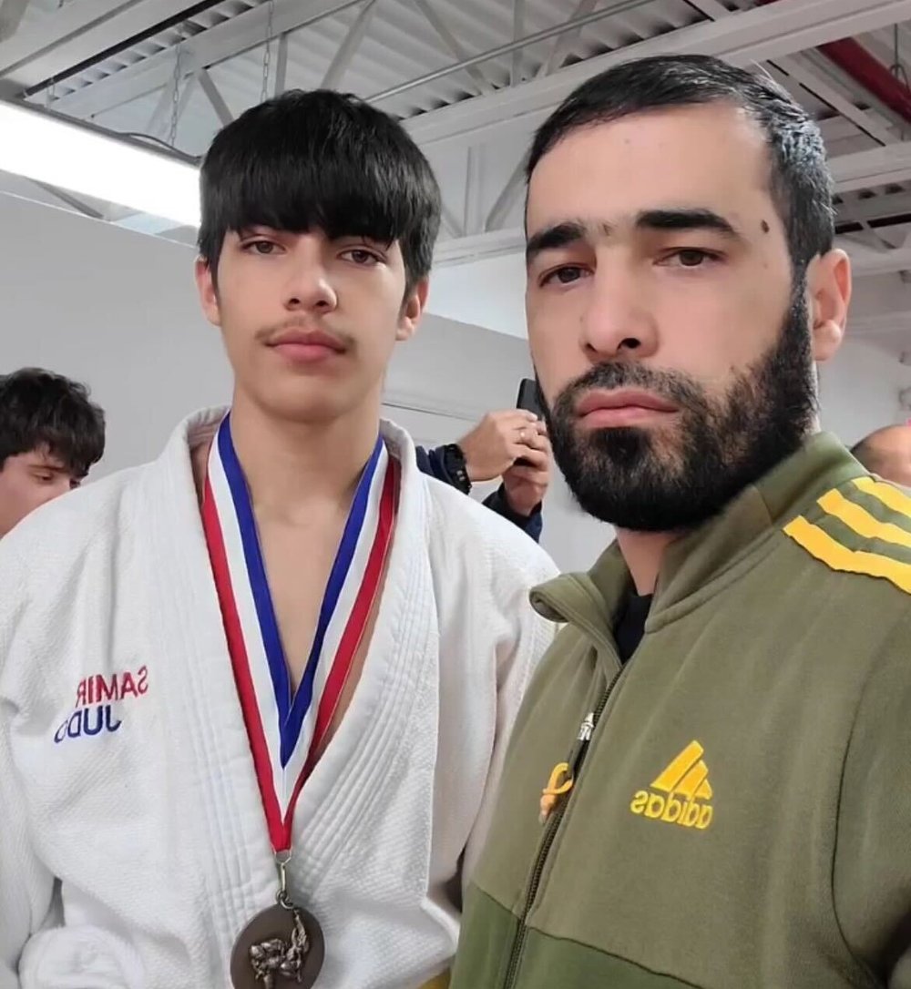 A boy with a medal around his neck stands next to his father.