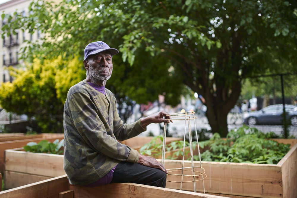 A gardener poses for a photo in front of vegetable beds.