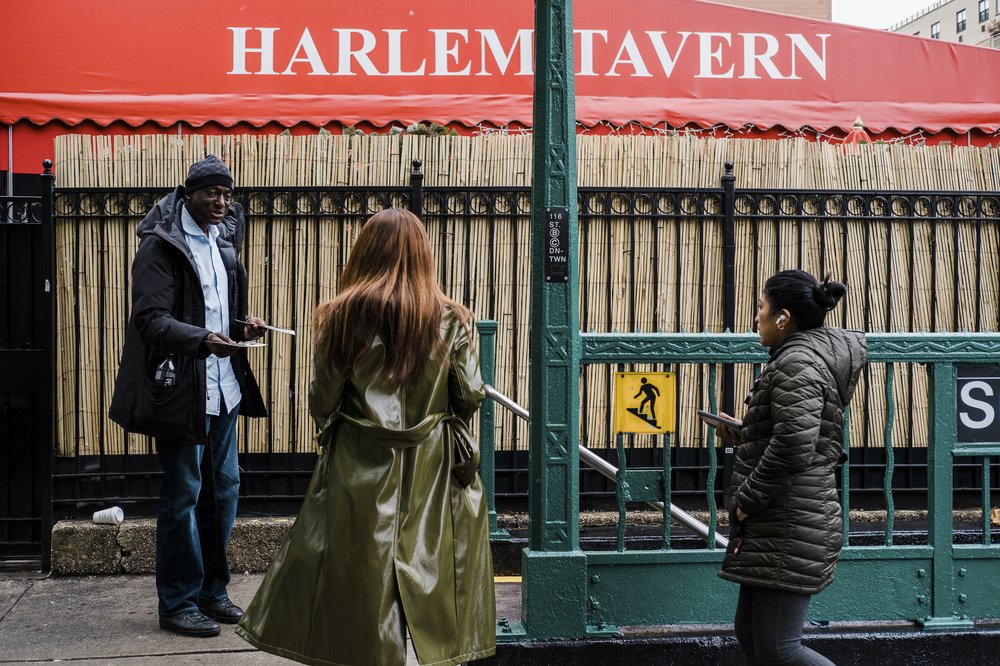 A person attempts to hand a pamphlet to two people just before they walk down the stairs and into the subway station.