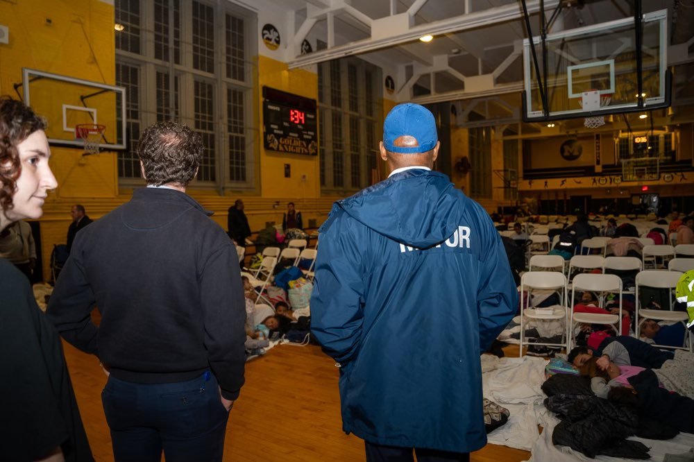 Mayor Eric Adams looks on as people sleep on the floor of a school gymnasium.