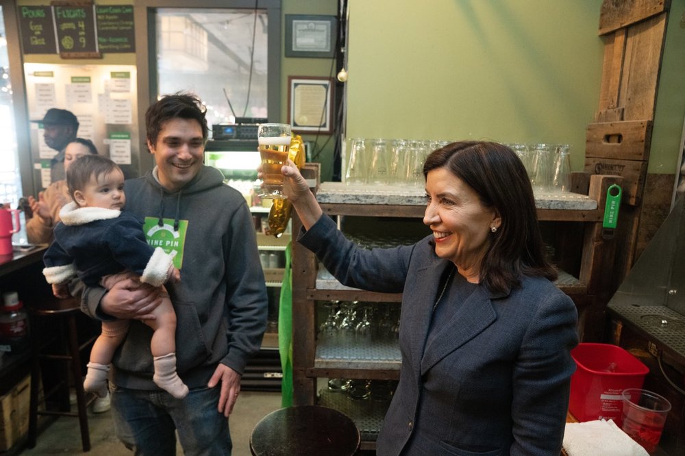 Gov. Kathy Hochul holds up a drink at a bar.