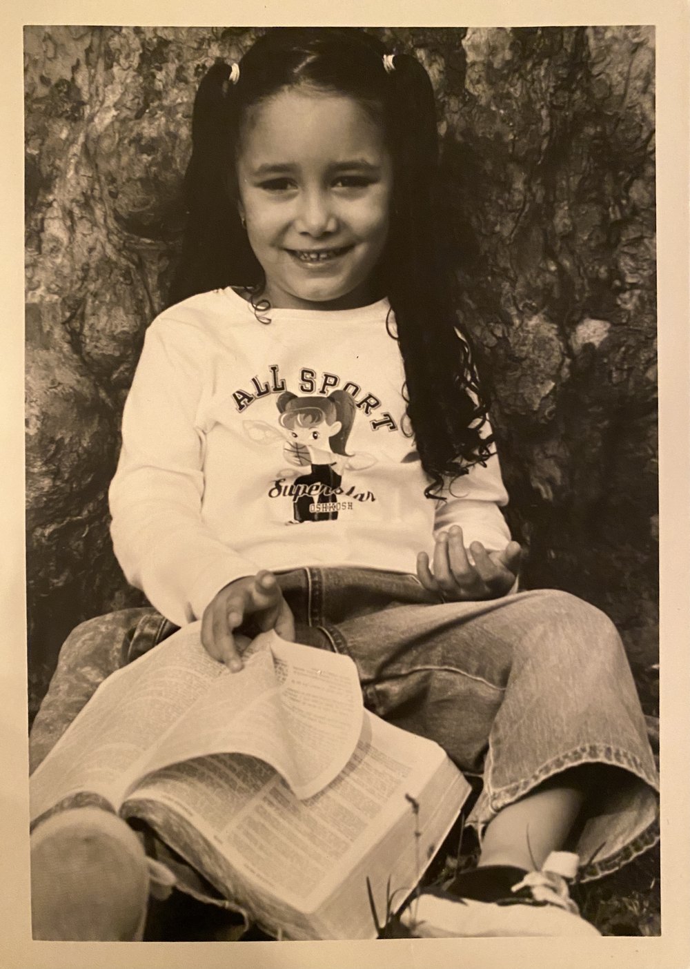 A young Genesis Reynoso is photographed with a thick book in a shirt that says All Sport Superstar.