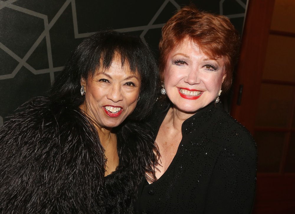 Two women wearing black pose for the camera.
