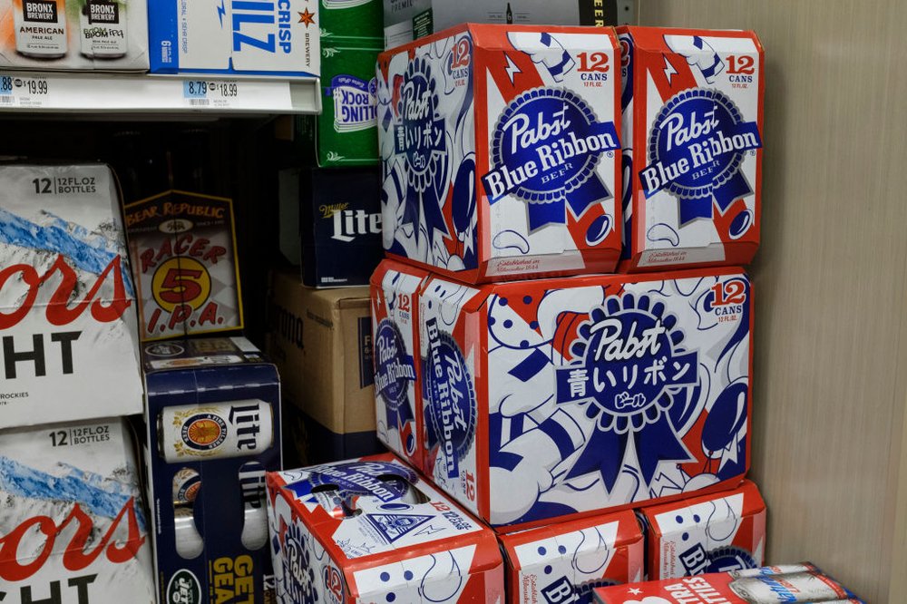 Stacks of Pabst Blue Ribbon 12-packs and other beers line the shelves of a convenience store.