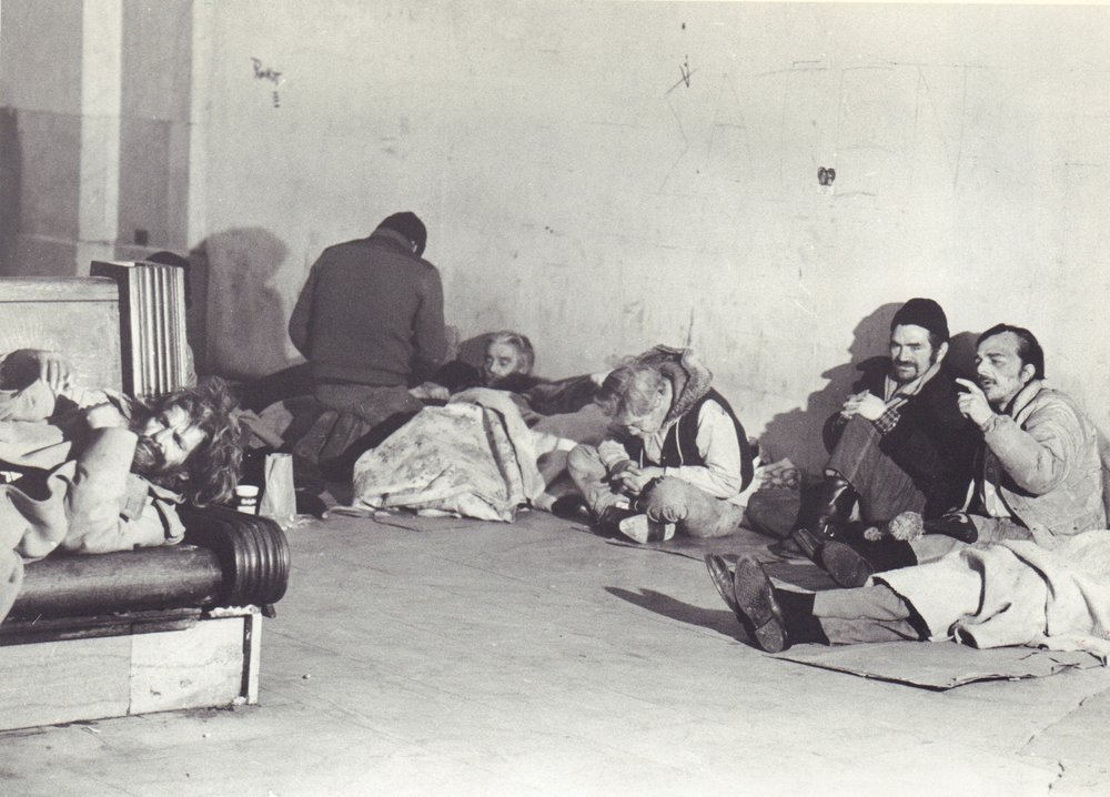 A black and white photograph of a group of homeless men sitting in Grand Central Station in 1985.