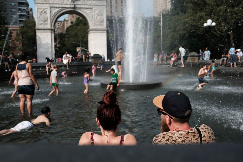 Dozens of people wade and dip their feet into the fountain at Washington Square Park during a heat wave in July.