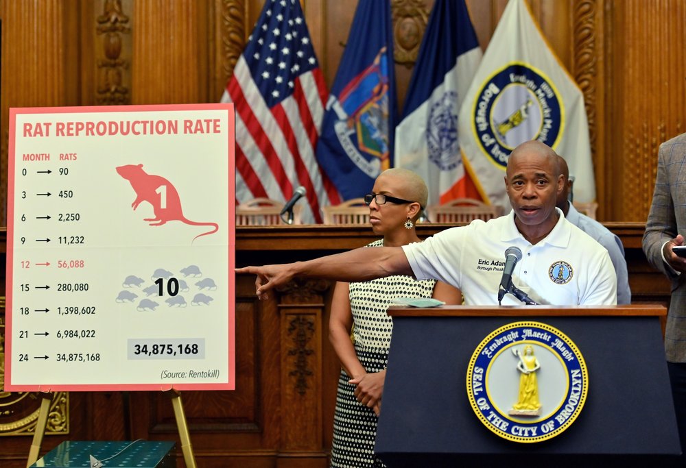 Then-Brooklyn Borough President Eric Adams points at a sign reading "rat reproduction rate" while delivering a speech.