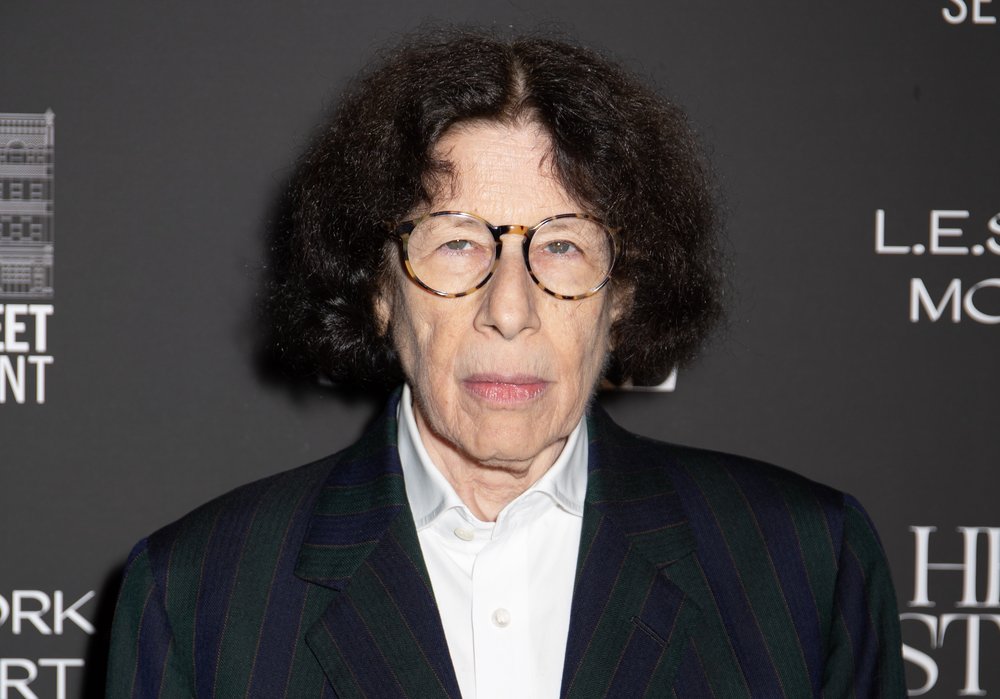 A person with a blazer and circular glasses.