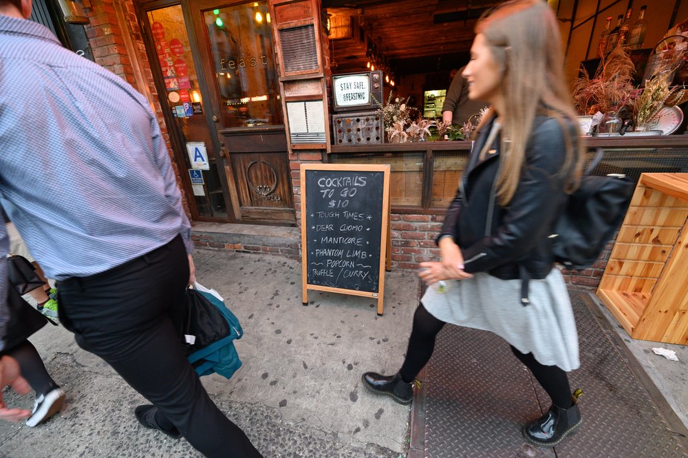 People walk past a sign advertising $10 cocktails to go.
