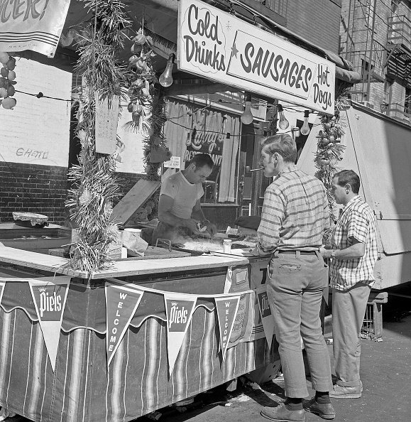 Two men wait in line for sausages.