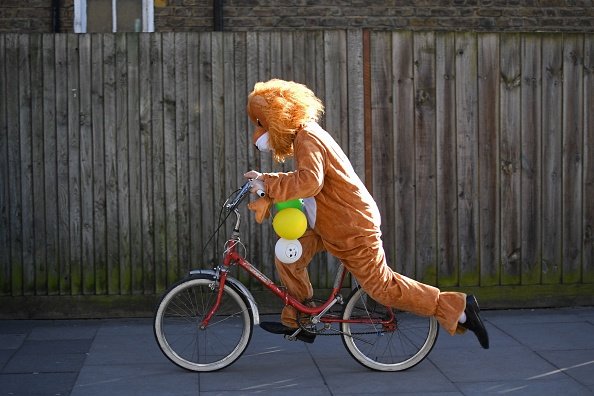 A man in costume as a lion rides a bicycle.