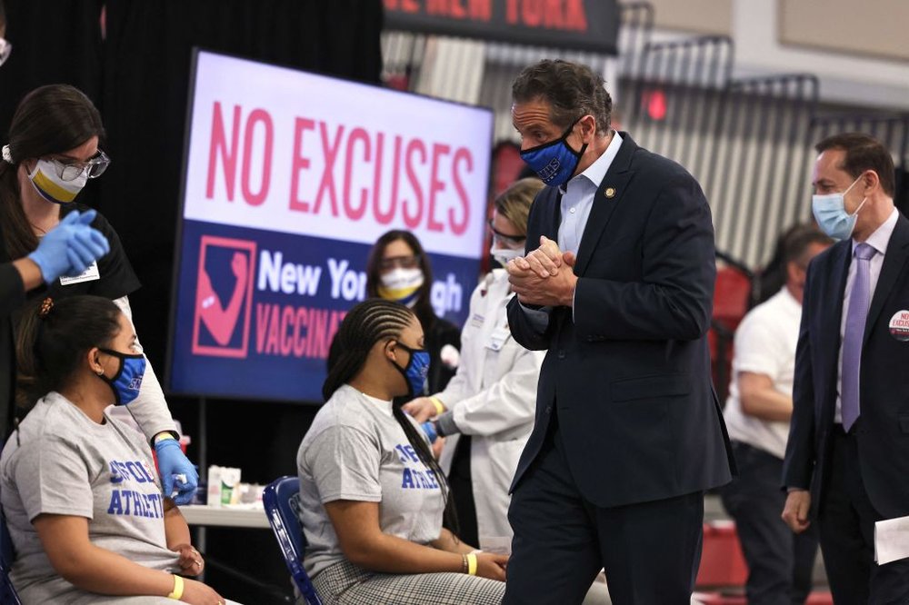 Former Gov. Andrew Cuomo, wearing a blue face mask and black suit, greets college students being vaccinated against COVID-19.