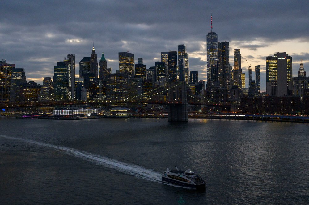 A photo of a ferry boat cruising along the East River with the Manhattan skyline in the background.