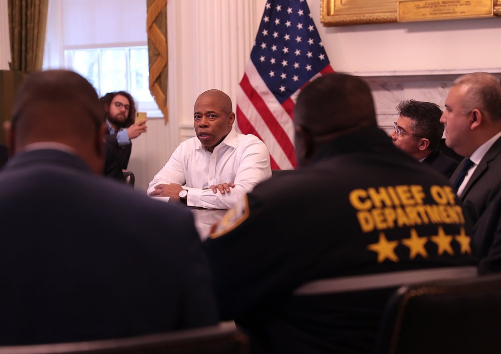 Eric ADams at a table. FOreground is a man's jacket saying CHief of Department.