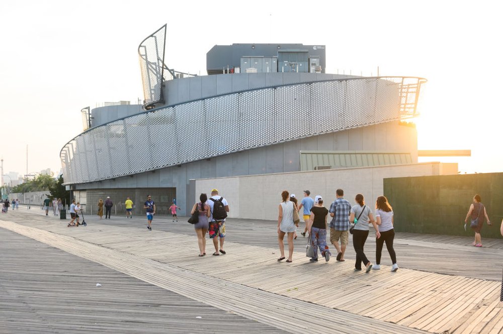 People walk on the Coney Island Boardwalk toward the New York Aquarium.