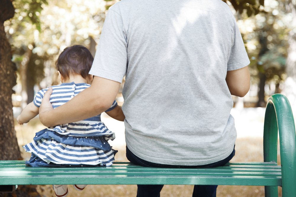 A man sits on a park bench with his daughter.