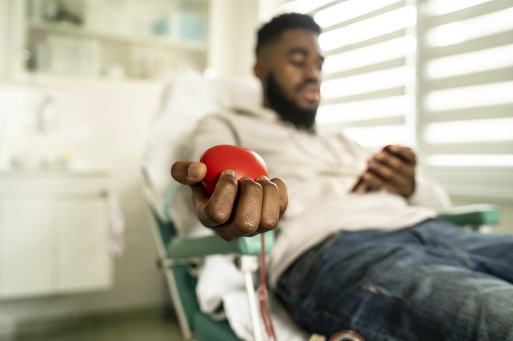 A man gives blood, squeezing a red ball.