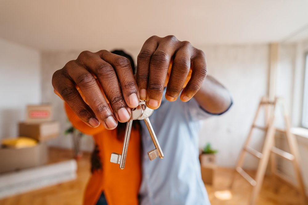 Two people's hands hold up keys to a home.