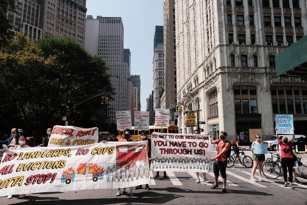A group of activists holding massive white signs saying "no landlord, no cops, all evictions gotta stop" block traffic in Manhattan.
