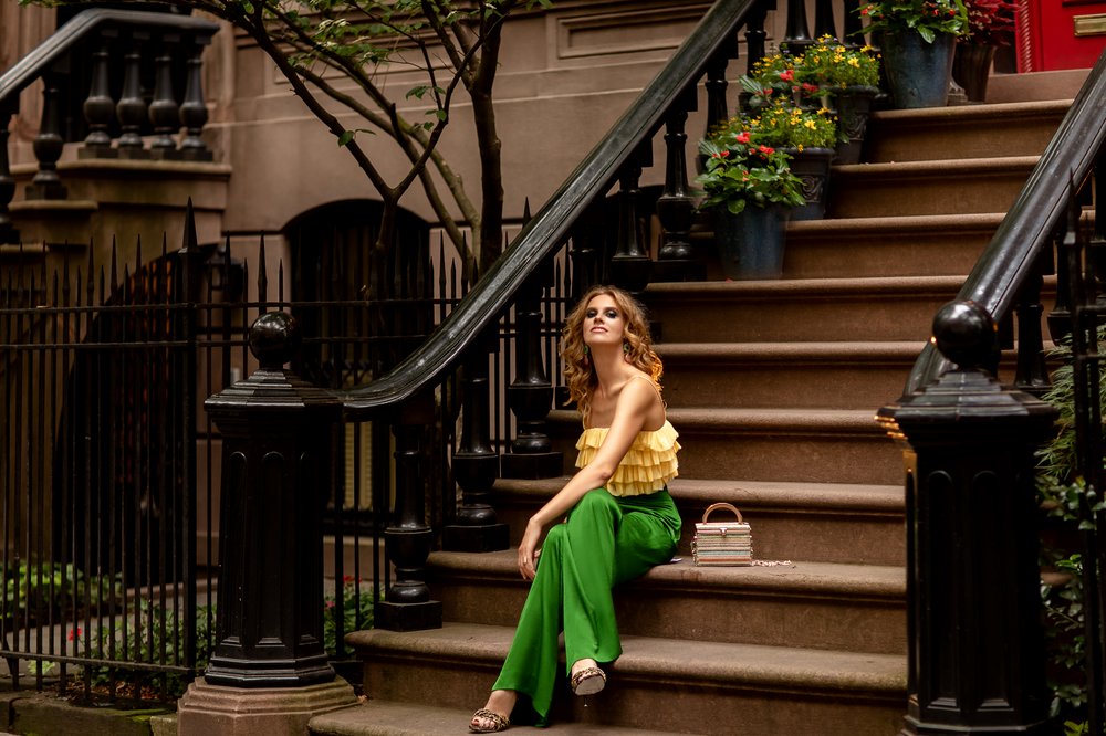 A woman sits on a stoop in green pants, a yellow shirt and heels.