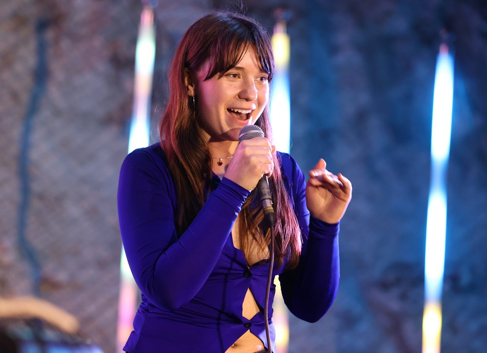 A woman singer wears a blue top and performs with a microphone.