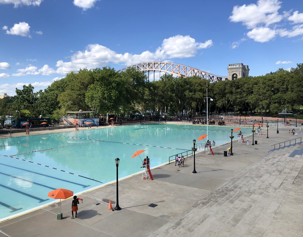 A photo of Astoria pool before it reopened in the summer of 2024. LIfeguards stand at the ready, and the giant Hell Gate Bridge looms in the background.