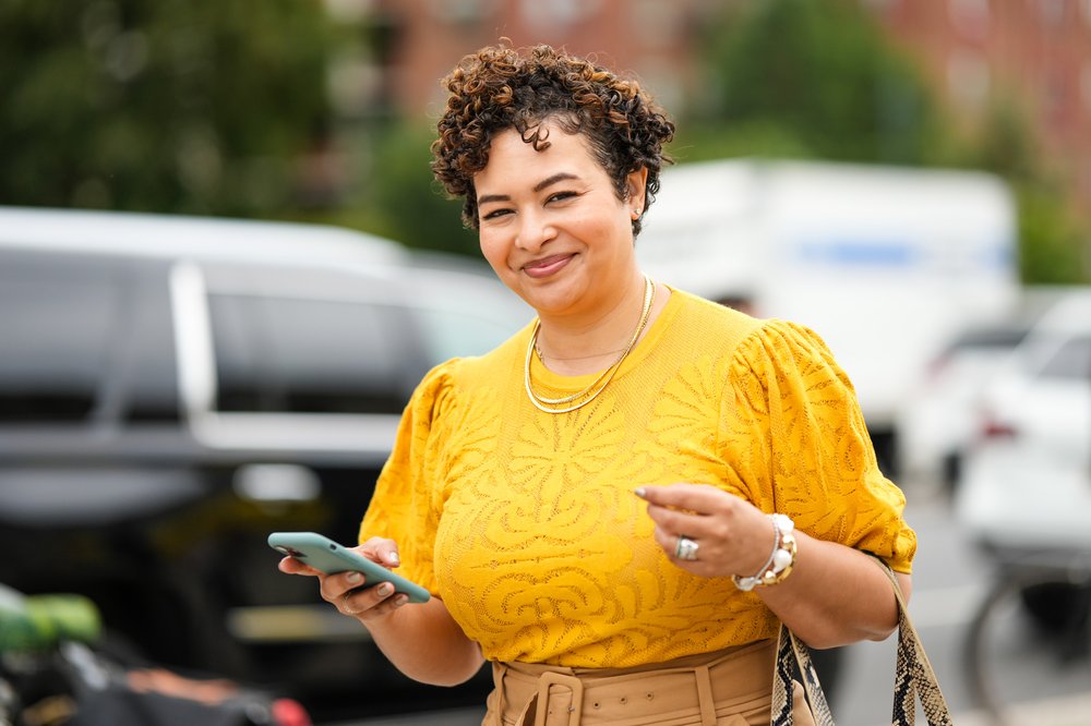 A woman in a yellow shirt holds her cell phone.