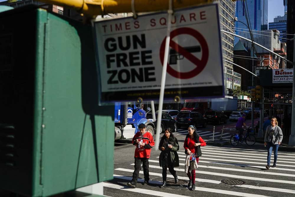 People walk near a Gun Free Zone sign displayed near Times Square.
