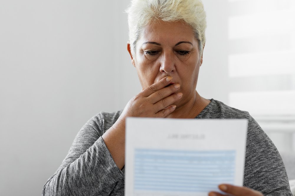 A woman looking at her electric bill, with her hand over her mouth.