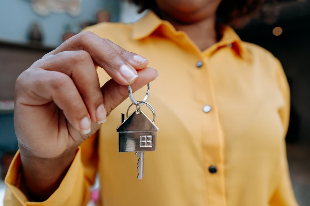 A hand holds out a key with a house shape on the keychain.