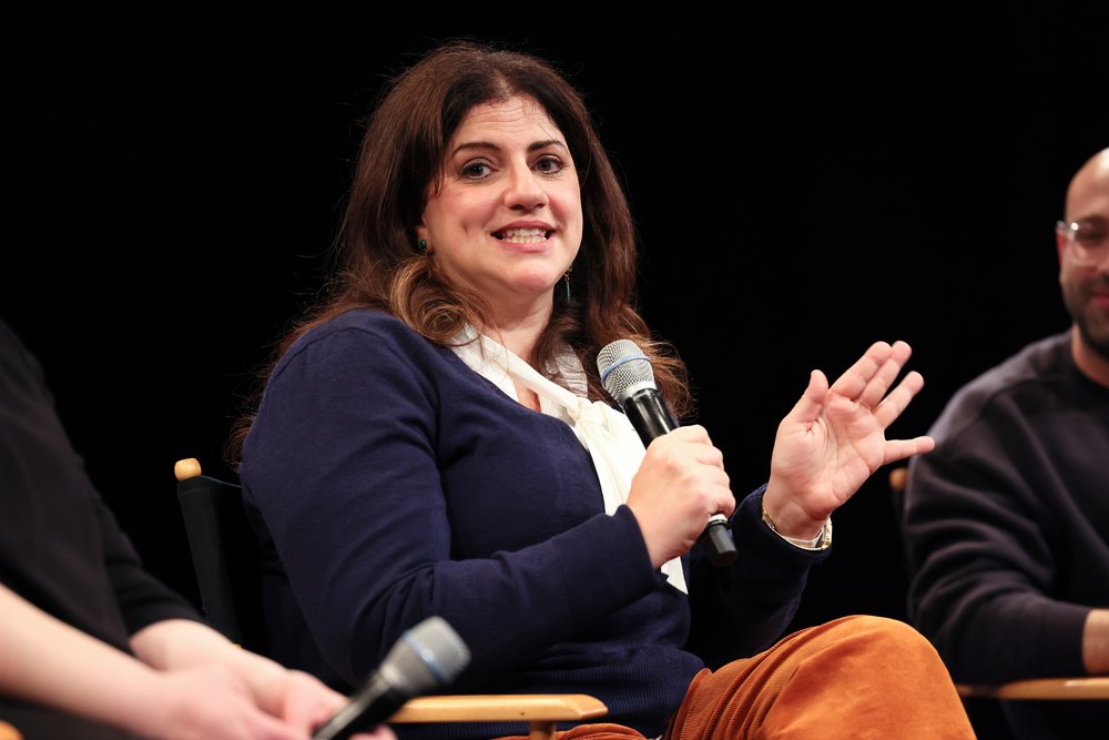 A person smiles on stage while holding a microphone.