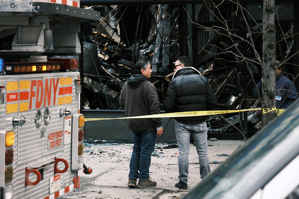 Fire officials and others gather outside of a Bronx supermarket the day after a 5-alarm fire tore through a market that fire officials are blaming on a faulty lithium-ion battery on March 6, 2023.