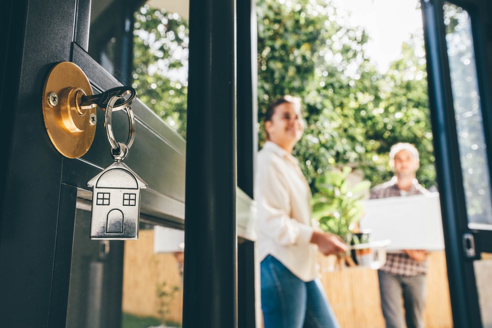 A man and woman enter a home with a key visible in the door.