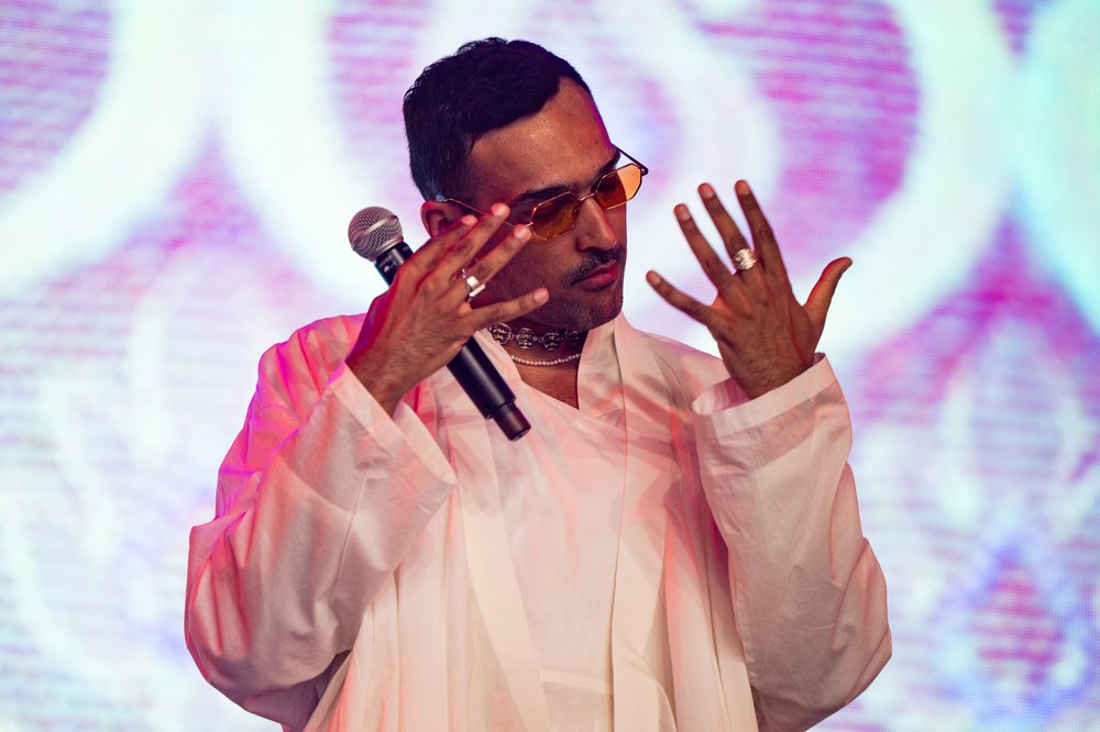 A singer in eyeglasses performing on an illuminated stage