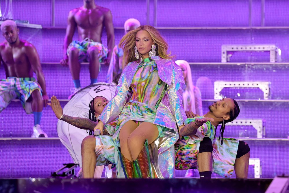 A singer in a colorful outfit performing onstage with dancers
