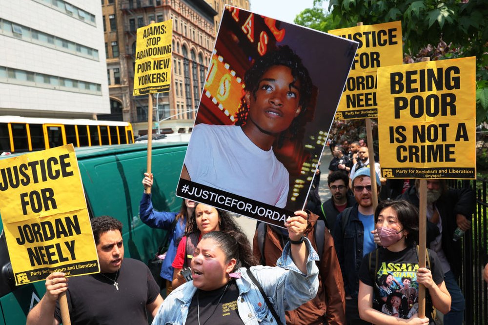 Demonstrators hold up signs and a picture of Jordan Neely saying "justice for Jordan Neely" and "being poor is not a crime."