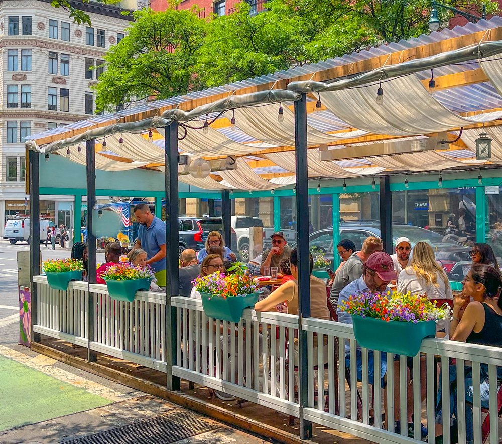 A group of people sit outdoors in a dining shed with flowerboxes and flowers.