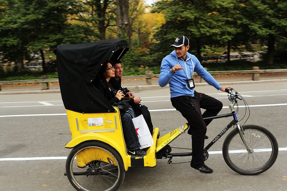 Two people in a pedicab, talking to the driver.