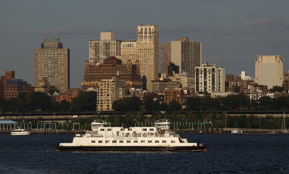 People ride on the Governors Island Ferry as the sun sets on the skyline of Brooklyn.