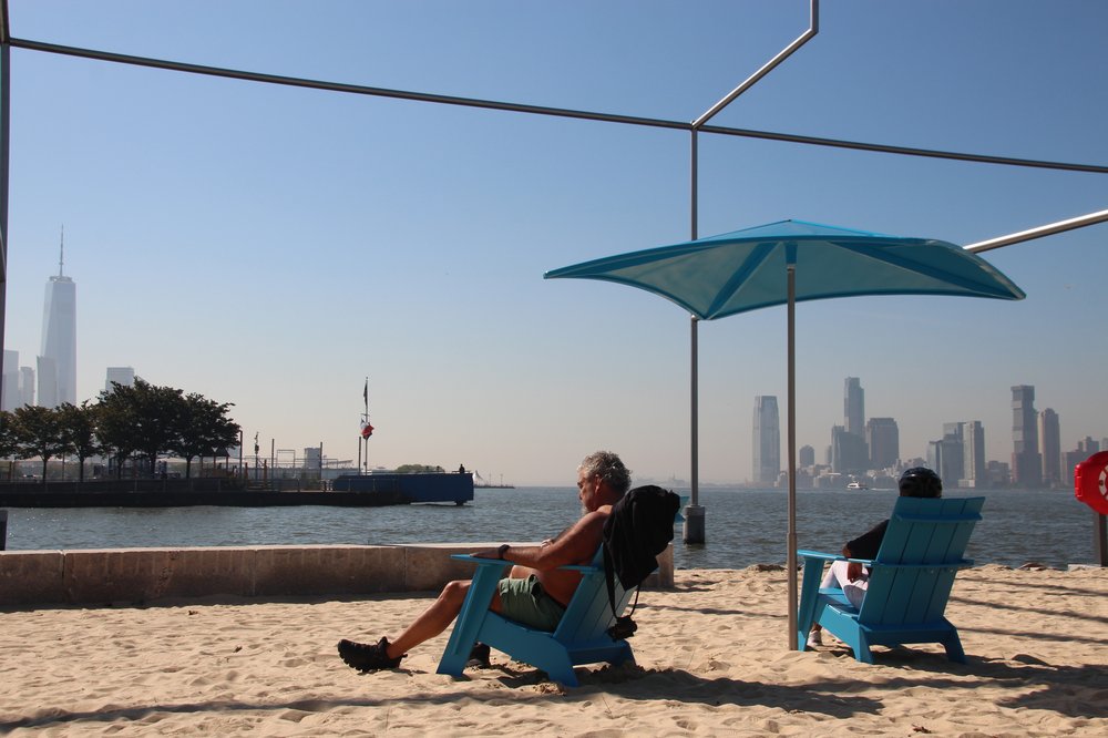 A man relaxes on a sandy beach overlooking downtown Manhattan.