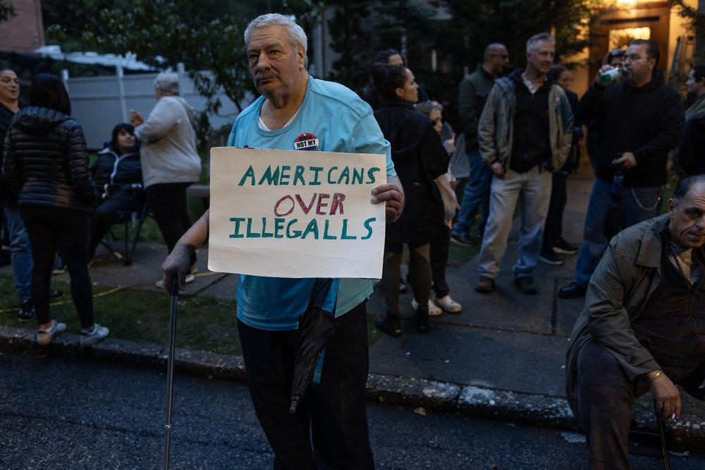 A man with a cane holding a sign reading "Americans over illegalls."