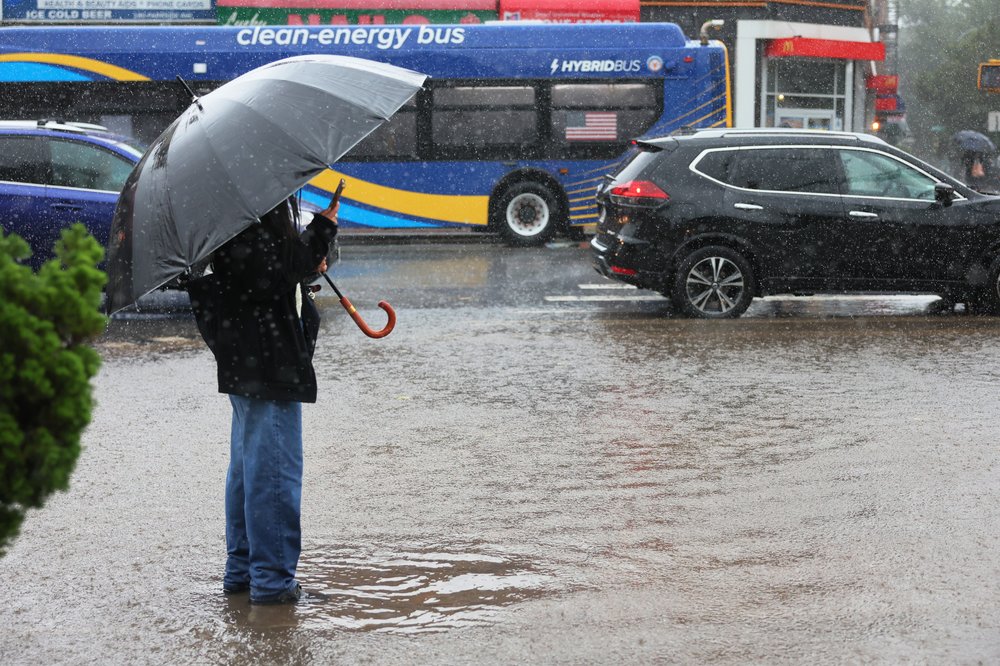 A person standing under an umbrella on a flooded sidewalk.