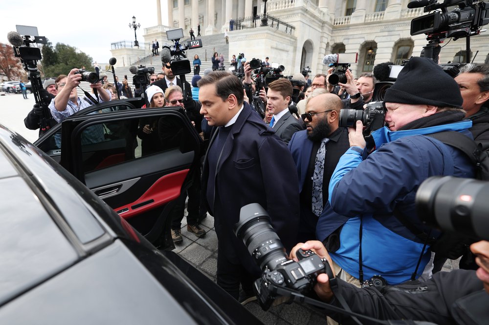 George Santos surrounded by journalists and cameras as he gets into a car following the vote to oust him from the House.