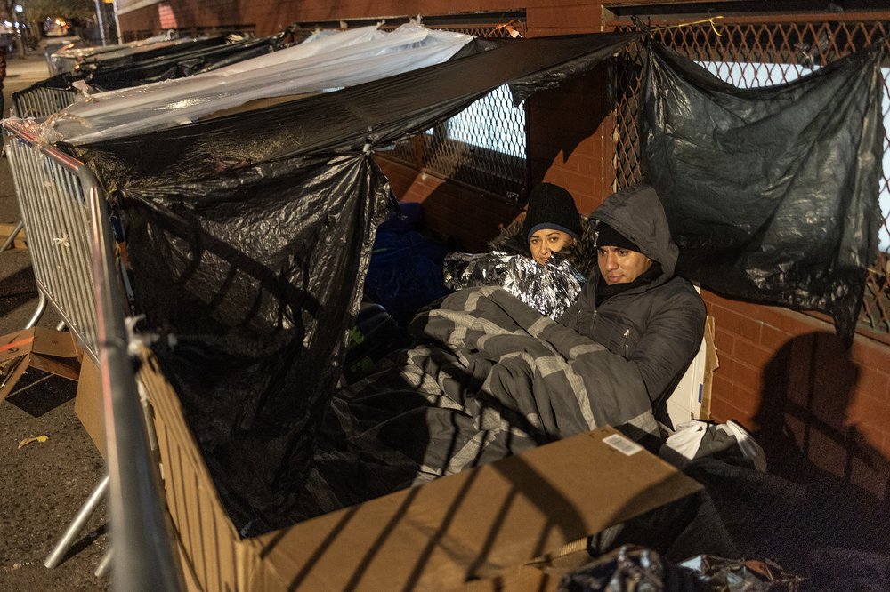 Migrants under blankets on a sidewalk.