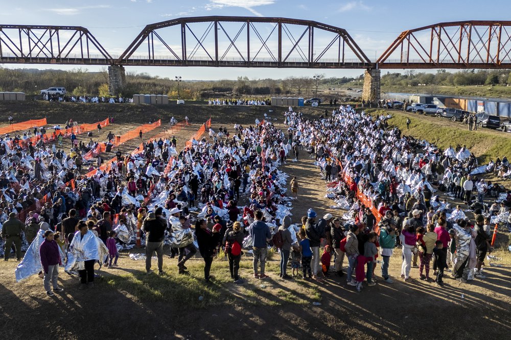Hundreds of people, many wearing reflective thermal blankets, await processing at a U.S. Border Patrol transit center in Eagle Pass, Texas.