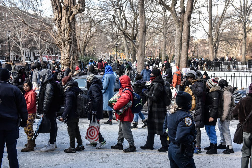 scores of people line up in the snow waiting to receive food and clothes donations in Tompkins Square Park.