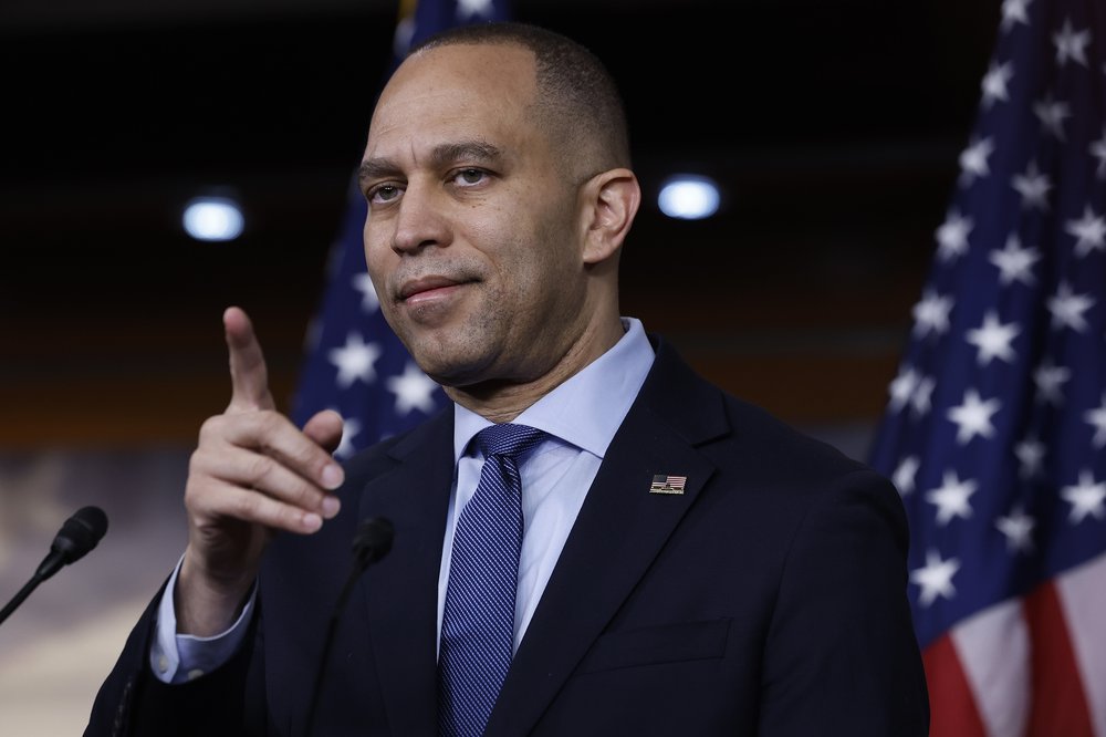 House Minority Leader Hakeem Jeffries points toward the camera with American flags in background.