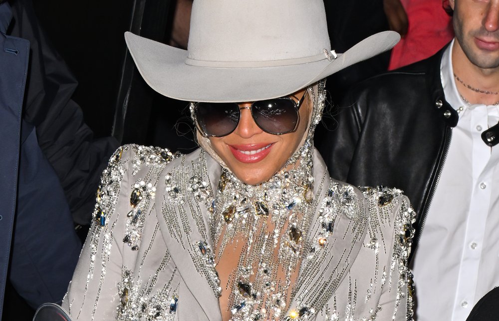 A women in a white country hat with a bedazzled jacket smiles at the camera.