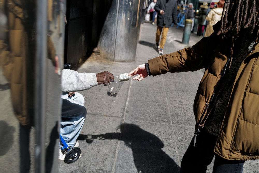 A person hands cash to someone sitting on the street.