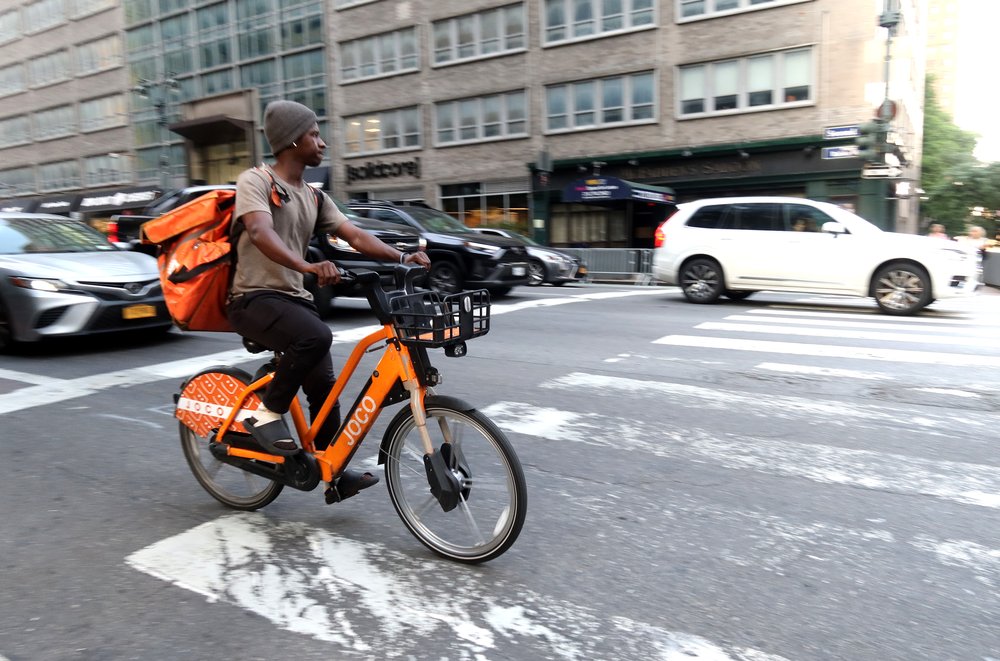 A delivery person for GrubHub rides an e-bike along Third Avenue.